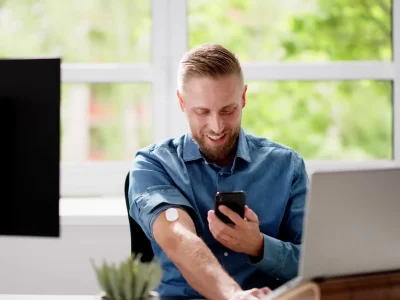 Hombre monitoreando sus niveles de glucosa con un sensor no invasivo mientras trabaja, optimizando su rendimiento profesional.